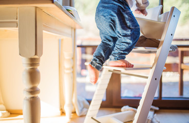 Toddler boy in a dangerous at home, climbing into highchair.