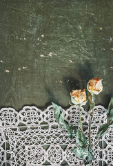 Vintage background with lace tablecloth and dry roses on old wood