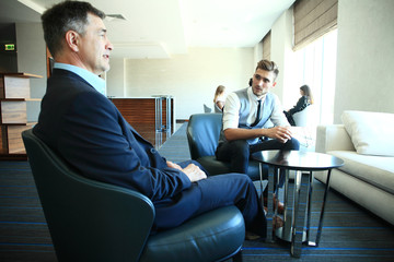 Mature businessman using a digital tablet to discuss information with a younger colleague in a modern business lounge.