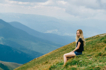 Fototapeta na wymiar Young girl relaxing and enjoying scenic view on top of mountain. Bliss and happiness. Beautiful summer nature landscape. Lonely young blonde teen traveler dreaming outdoor on vacation. Romantic mood