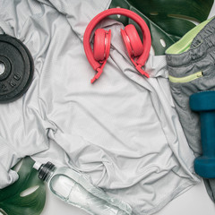concept sports lifestyle, sportswear, headphones, dumbbells, lined on a white background, with a bottle of water and tropical leaves, space for text
