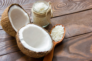Fototapeta na wymiar fresh coconut cracked in half on a wooden table with coconut chips in a glass jar and in a wooden spoon with a place for writing