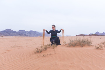 Fototapeta na wymiar A young woman with blond hair in a long dark blue dress is playing with sand. Wadi Rum Desert Jordan