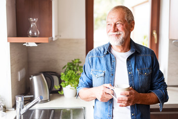 Happy senior man holding a cup of coffee in the kitchen. - Powered by Adobe