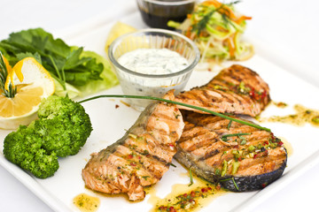 Steaks of salmon, grilled. Served with vegetables and spices on a white plate