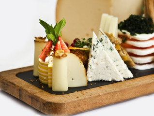 Cheese plate: roquefort with blue mold, cheddar, smoked cheese, mozzarella on a wooden board. Decorated with red currant berries, strawberries and mint