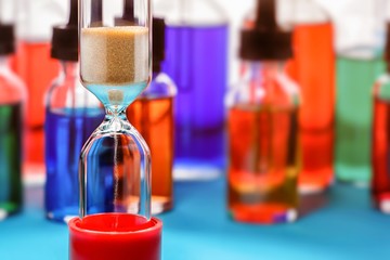 Closeup of hourglass on blurred bottles background. Toned