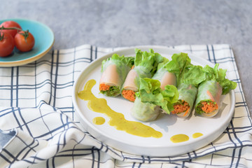 Thai healthy food : Close up of homemade mixed fresh vegetable salad roll in noodle on white dish with  seafood dipping sauce.