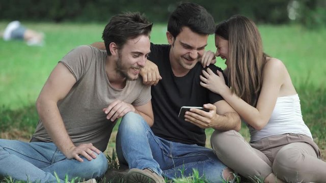 laughter, joy, friendship - three friends at the park watch the smartphone laugh