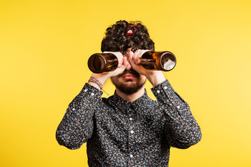 Studio portrait of a young man holding bottles on a yellow background.