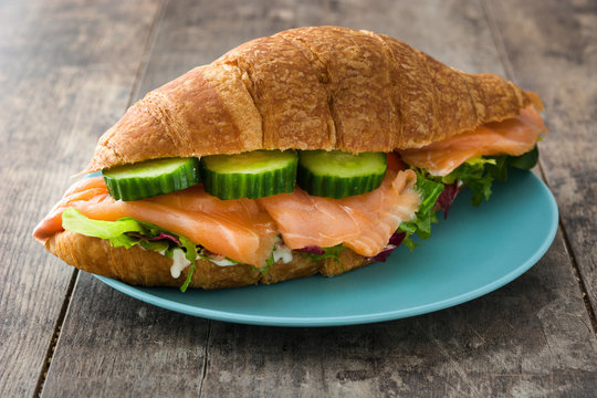 Croissant sandwich with salmon and vegetables on wooden table