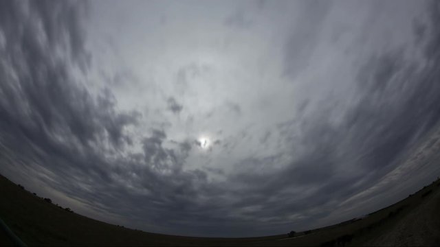 Fisheye lens view of gray storm clouds rushing over dark prairie, time lapse