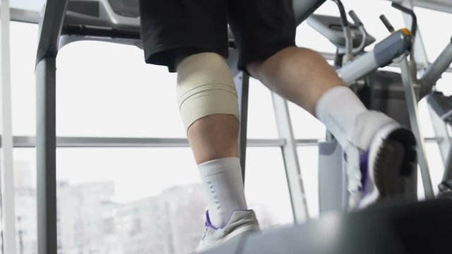 Male with injured leg muscle walking on treadmill in gym, recovery, will power