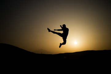 Athlete jump high with energy. Sportsman silhouette on sunset sky. Man training on natural landscape. Workout in summer dusk. Sport, wellness and bodycare concept