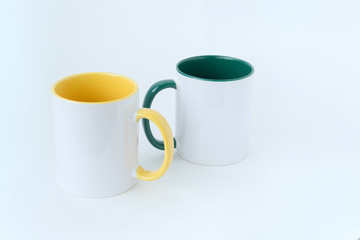 Two white mugs, with a green and yellow handle on a white background.  Isolated.  