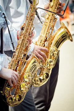 Two musicians play saxophones on the street.
