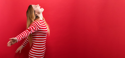 Happy young woman with her arms outstretched on a red background