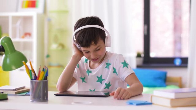 childhood, technology and leisure concept - smiling little boy with tablet pc computer and headphones listening to music at home
