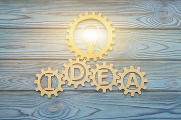 IDEA burning lamp in gears composed of puzzle pieces, on a blue background of wood texture. Business concept, teamwork, cooperation, strategy, innovation, creativity