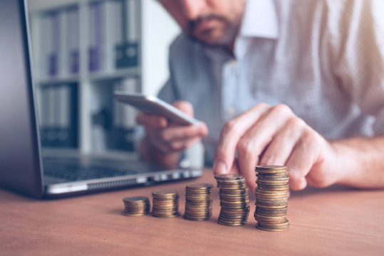 Businessman using smartphone with stacked coins in foreground