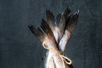 Raw fish tails tied with rope with bow on dark background. Selective focus
