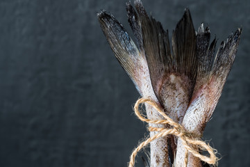 Raw fish tails tied with rope with bow on dark background. Selective focus
