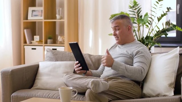technology, people and communication concept - happy man with tablet pc computer having video chat at home