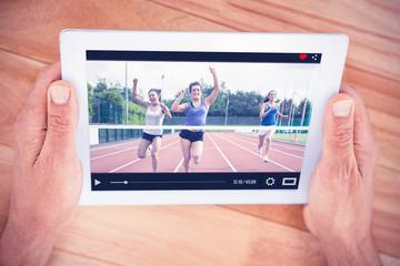Athletes celebrating as they cross finish line against hands holding blank screen tablet
