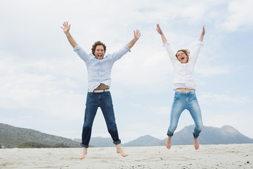 Fototapeta na wymiar Cheerful young couple jumping at beach