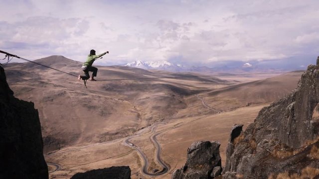 Slackliner resting on tightrope between two rocks, Snowy mountains of the Huascaran park on the background, Peru. Slow motion