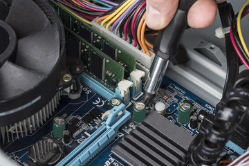 the hand of a computer engineer with a screwdriver repairs the motherboard
