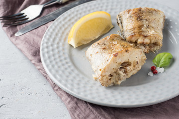 Baked Pollock fish with lemon and spices on a plate Napkin on the table