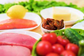 Raw appetizing fillet of tuna on a table with a yard of Greek salad with salmon and lemon cucumbers and tomatoes as well as cheese. The concept of a delicious and healthy home-made meal