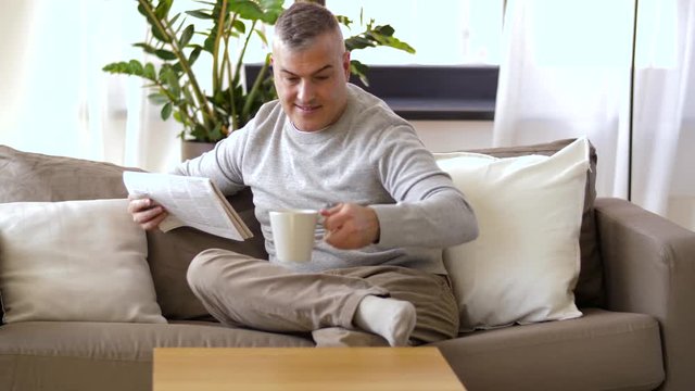 leisure, information, people and mass media concept - man reading newspaper and drinking coffee at home