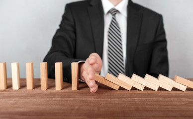 Close up of businessperson stopping dominoes from falling on desk.