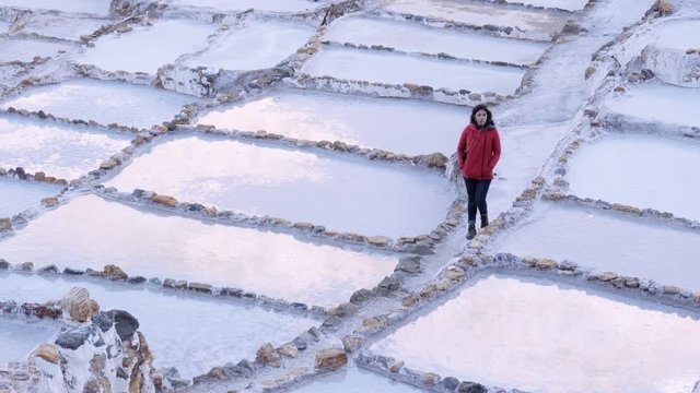 Woman walking on the corridors of salt  ponds during the marvelous sunset. Maras salt terraces in Peru. 4k