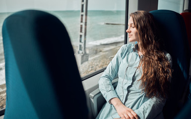 smiling girl looks out the train window. Attractive lady in turquoise dress sits in a train.
