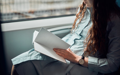 Cute girl is reading a book in a train. The lady turns the pages of the book. Girl rides on a train