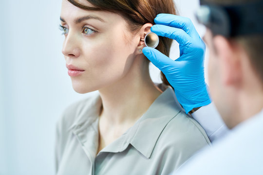 Portrait of unrecognizable doctor examining ears and hearing of beautiful young woman