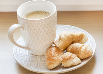 coffee in a white Cup with white saucer and croissants on wooden background