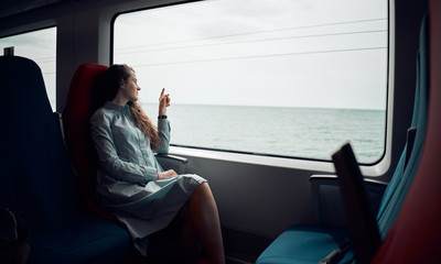 Thoughtful girl was going home on the train. Beautiful view from the train window to the sea. The...
