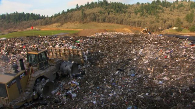 Two bulldozers moving garbage at a landfill