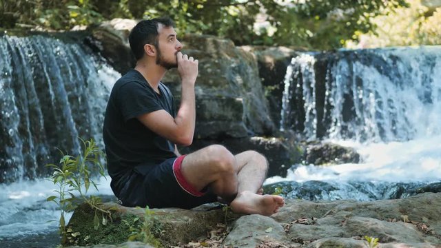 Young man praying alone near the waterfall: religion,meditation,nature