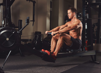 Fototapeta na wymiar Handsome muscular fitness male doing exercise on the rowing machine. 