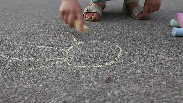 Child girl draws with colored chalk on asphalt pavement close up outdoor