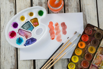 Watercolor paints, paper and paint brushes on wooden surface