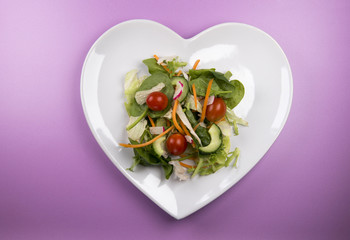 Traditional salad on a heart shaped plate on a pink background