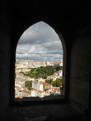 Bright city view with red roofs and beautiful cloudy sky through arched window in old stone wall, Lisbon, Portugal