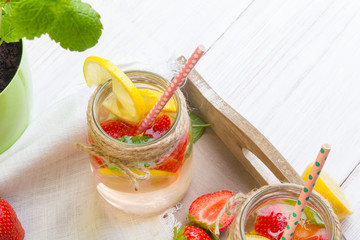 Mineral  water with fresh strawberries, lemon  and mint in jar on a white wooden background, copy space
