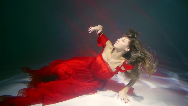romantic blonde woman is stretching her body on a bottom of sea, floating underwater in red dress